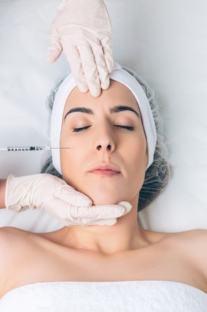 Aesthetician's hands in latex gloves injecting botox into female's cheek in a beauty salon