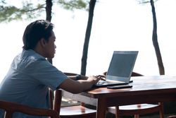 Back View Asian Young businessman work at outdoor with laptop blank screen. Concept of remote and freelance work. Young successful man wearing casual blue cloth.