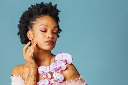Studio beauty shot of a Black woman with purple flowers and her eyes closed