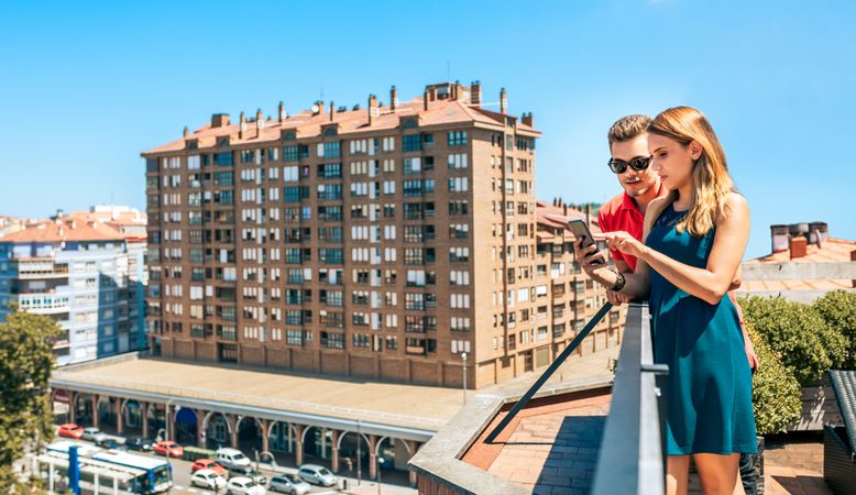 Young couple looking mobile in rooftop on a summer day