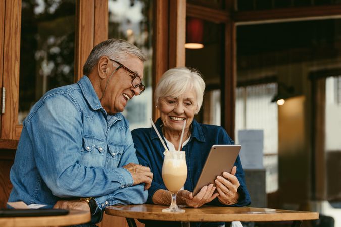 Cheerful couple sitting at cafe table and looking at photos on a digital tablet