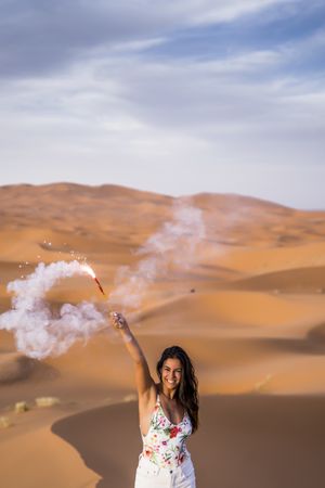 Happy woman holding firework in desert