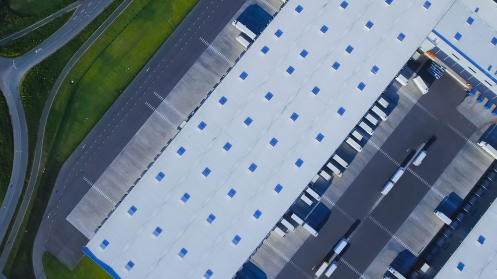 Aerial Shot of Truck with Attached Semi Trailer Leaving Industrial Warehouse Loading Area where Many Trucks Are Loading