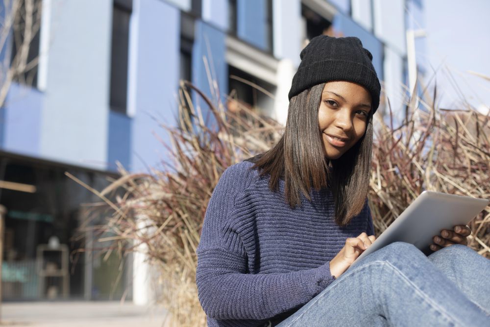 Female in hat and sweater sitting outside with tablet