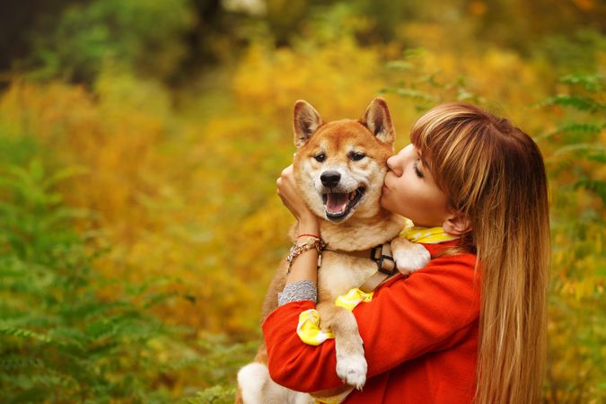 Female in red coat holding her cute affectionate shibu dog standing in field