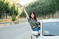 Smiling brunette female waving straw hat outside passenger window