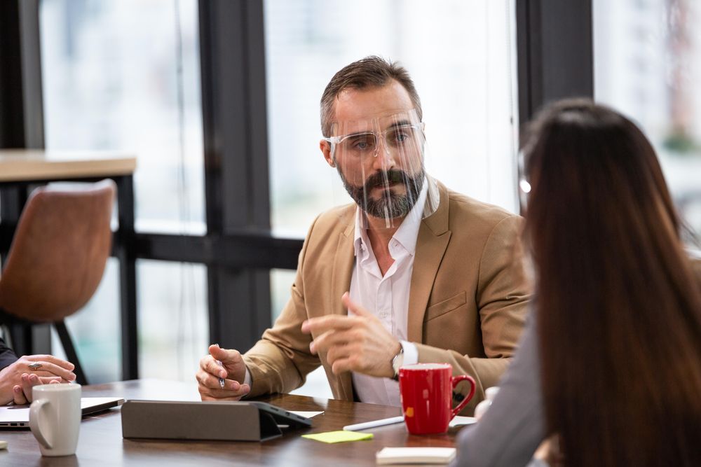 Business man wearing face shield brainstorming with team in co-working space