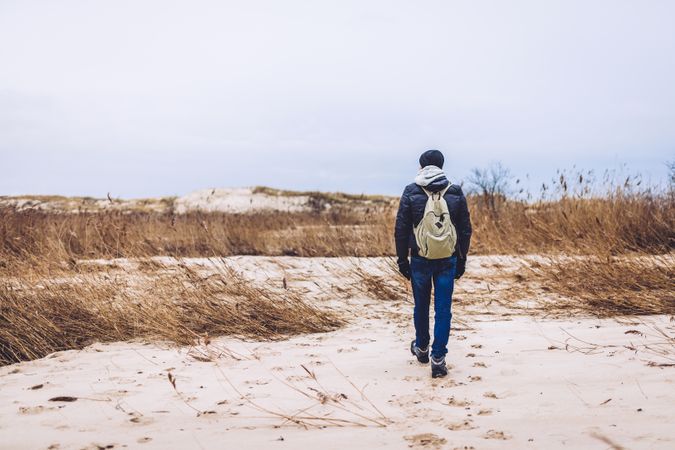 Man walking between sand field with dry grass