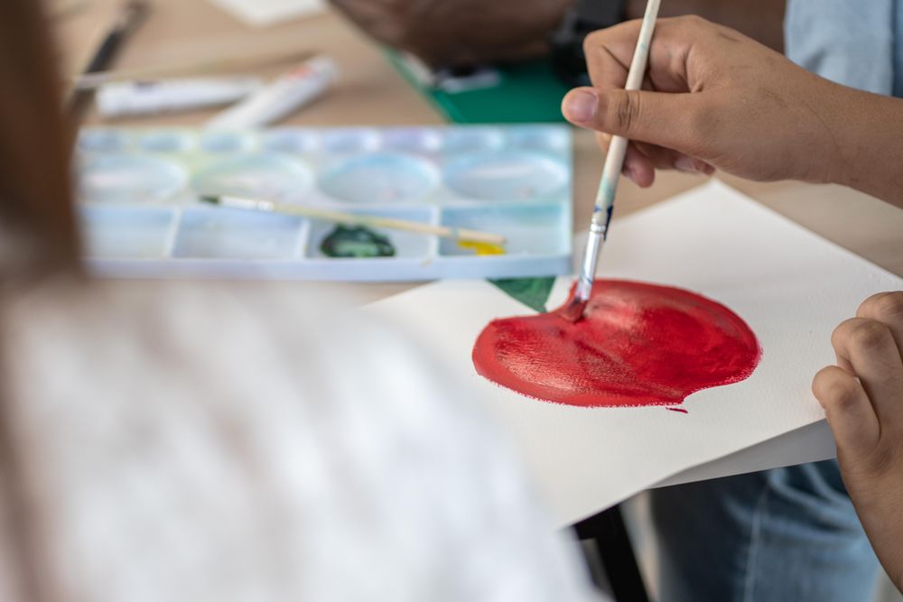 Close up of classroom table with students sitting painting an apple