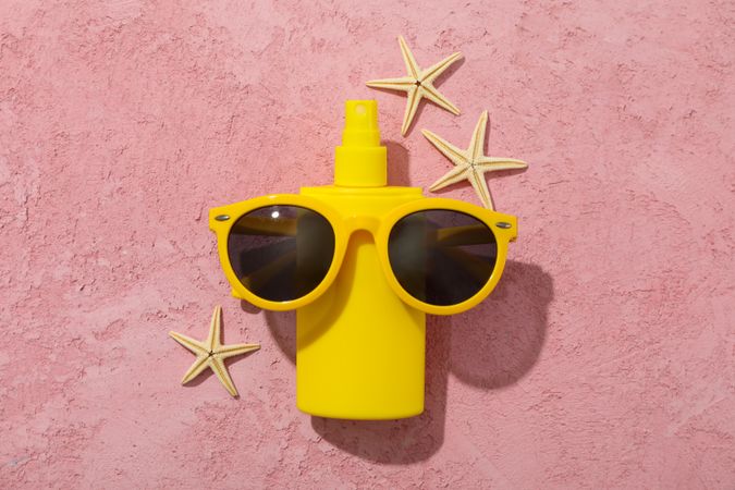 Sunscreen, sunglasses and starfishes on pink background