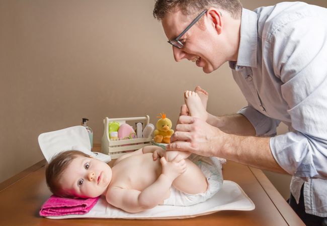 Father playing with baby during diaper change