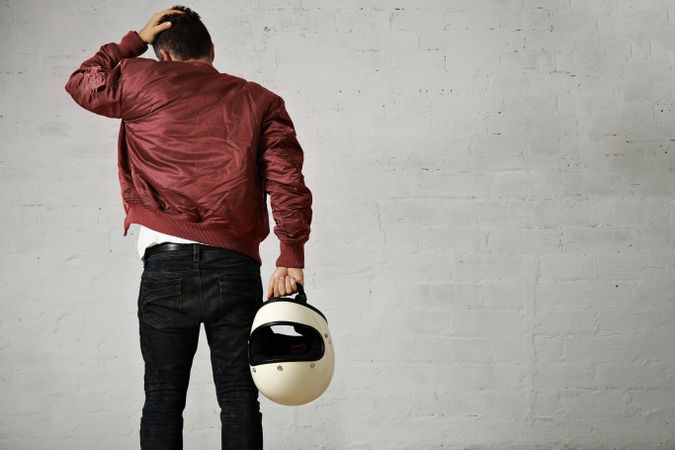 Rearshot of man looking down wearing dark red leather jacket holding helmet in hand