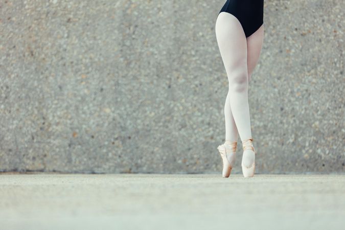 Young woman wearing leotard, tights, and pointe shoes outdoors