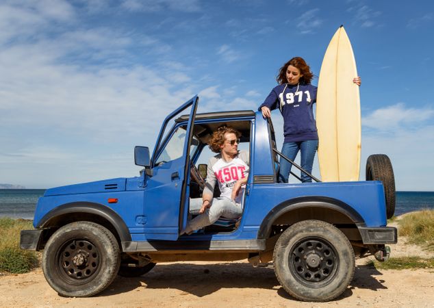 Guy with surfboard and woman on roof of car