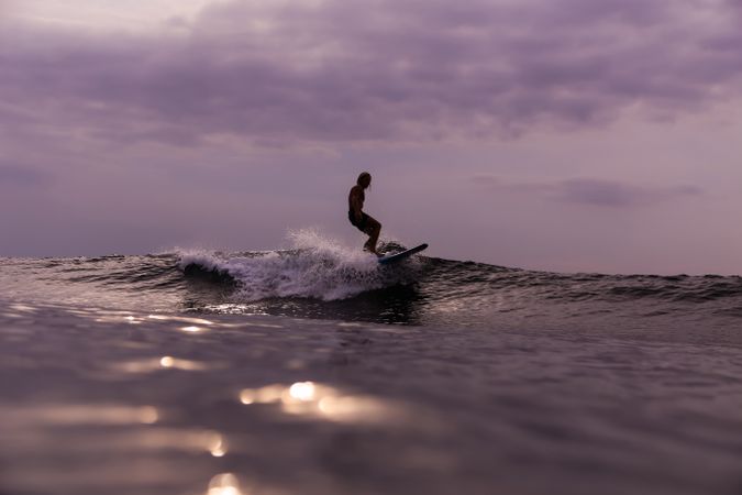 Man on surf board on waving water at sunset