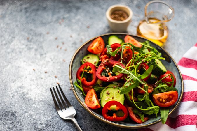 Healthy vegetable salad with organic cucumber, tomatoes, bell pepper, arugula and flax seeds on stone background