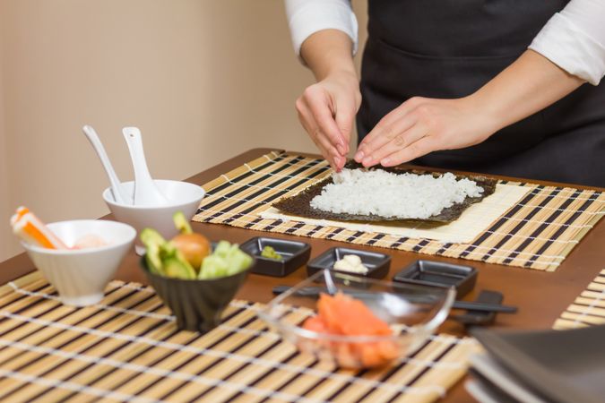 Hands of woman chef preparing sushi rolls with rice on a nori seaweed sheet