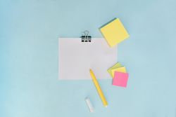 Flat lay of pens and note pad paper on blue background