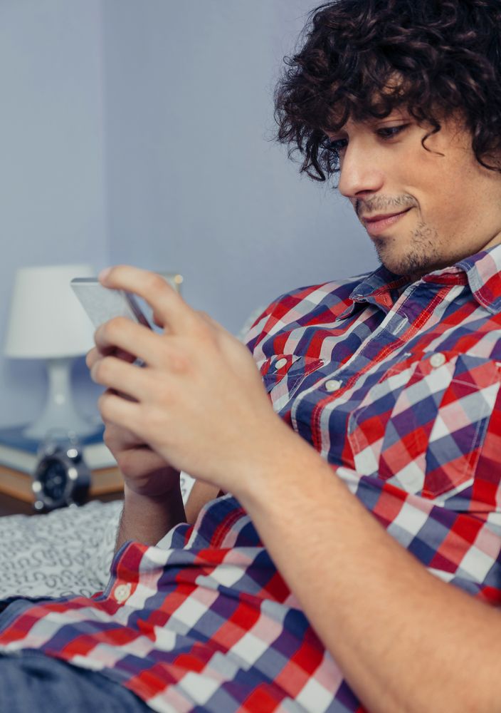Young man reading smartphone in bed