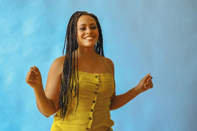Smiling female with long braided hair and both hands up in yellow one piece