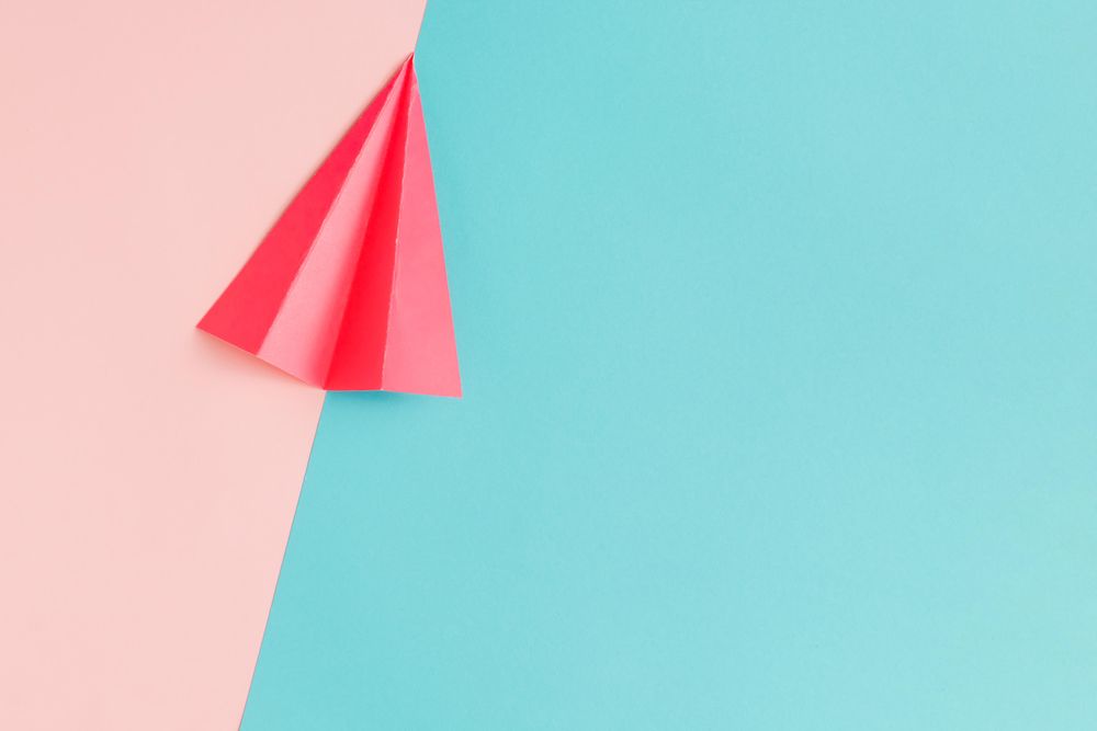 Red paper airplane on pastel pink and blue background