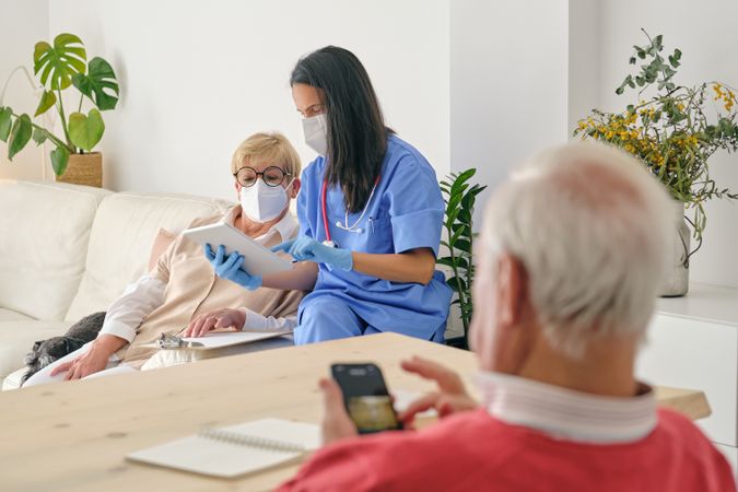 Doctor sharing tablet with mature patient against man at home