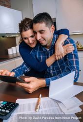 Woman holding man as they organize bills together in their kitchen, vertical 5kqEjb
