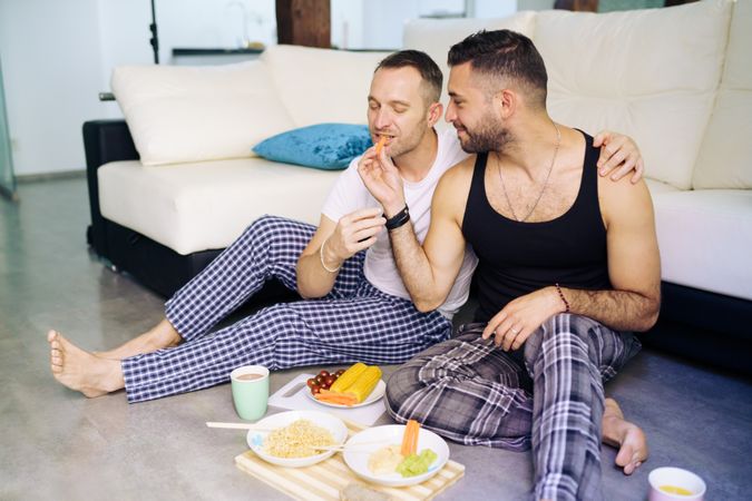 Happy male couple enjoying dinner at home sitting on floor