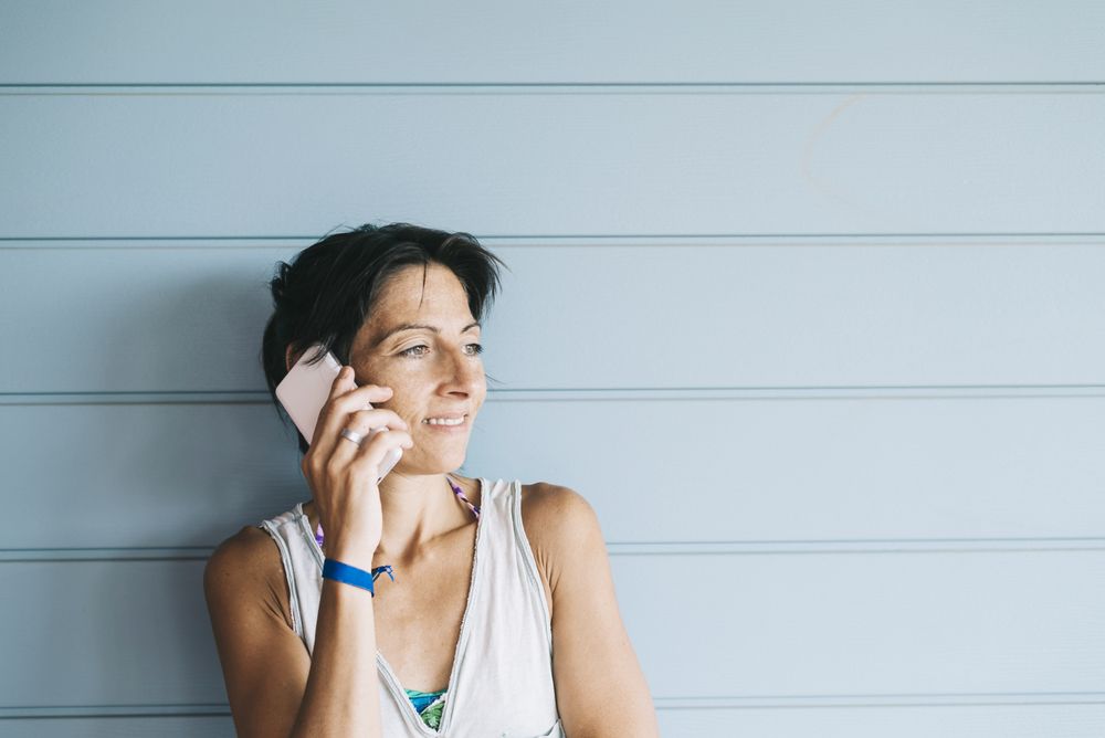 Adult female in summer dress talking on cell phone while leaning against wood paneled wall
