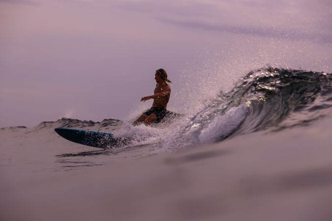 Man on surf board on waving water at sunset