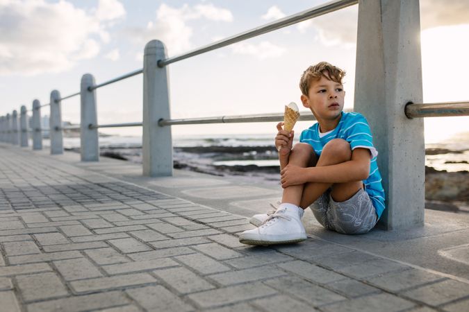 Boy eating an ice cream sitting on a pier with setting sun in the background