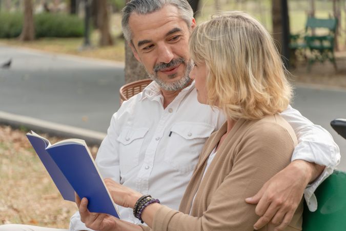 Male and female older couple sitting together and reading on park bench