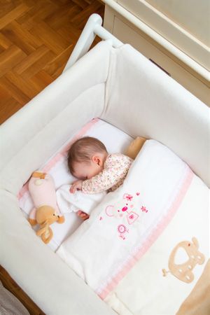 Newborn baby girl sleeping in a cot with pacifier and toy