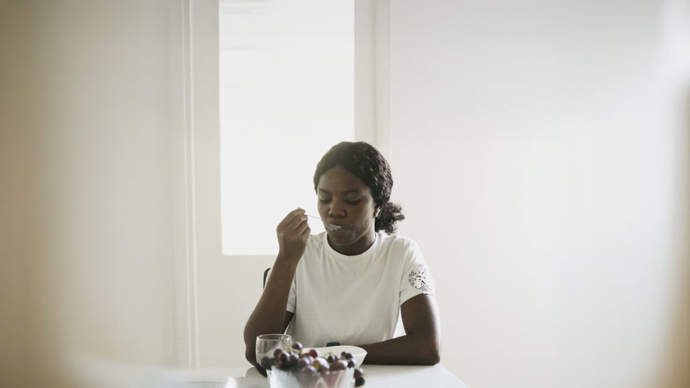 Black Woman Sitting at Dining Table Enjoying a Nutritious Snack.