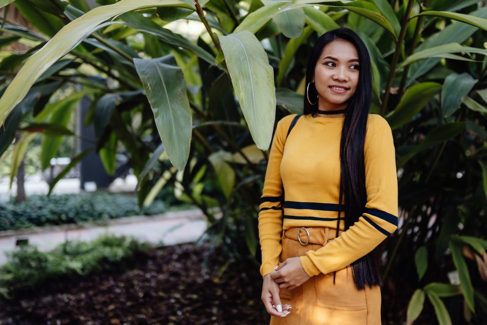 Stylish long haired Asian woman standing in park with flowers
