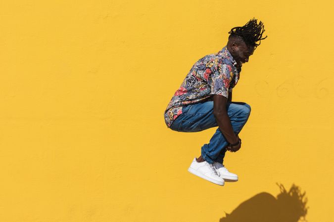 Energetic Black man jumping near yellow wall