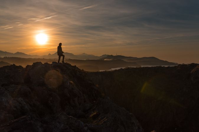 Traveler on high coastal cliff in sunset