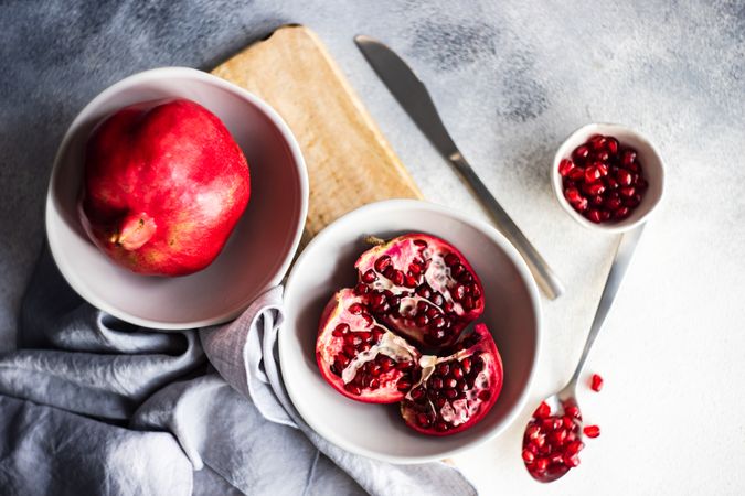 Fresh cut pomegranate on light plate with bowl of seeds with copy space