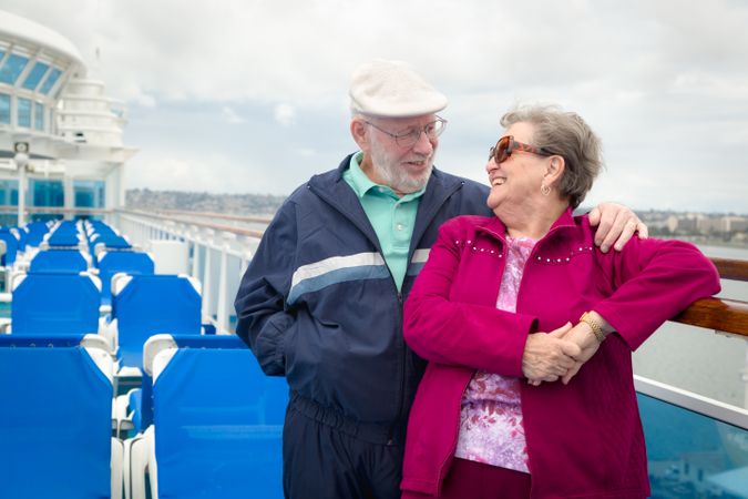Grey Haired Adult Couple Enjoying The View From Their Passenger Cruise Ship Railing.