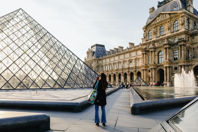 Back view of woman in dark coat standing outside the Louvre museum in Paris, France