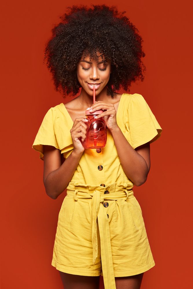Charming bright Black woman drinking beverage