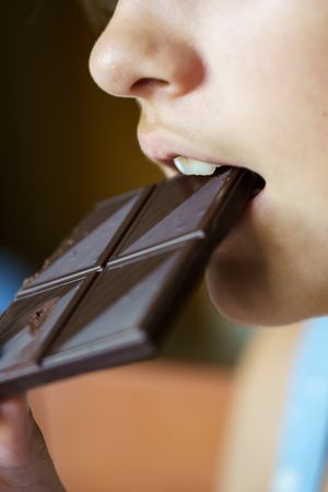 Anonymous girl biting yummy chocolate bar at home