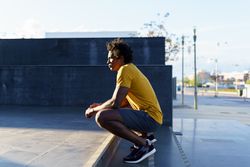 Man crouched down looking into the sun on stairs outside