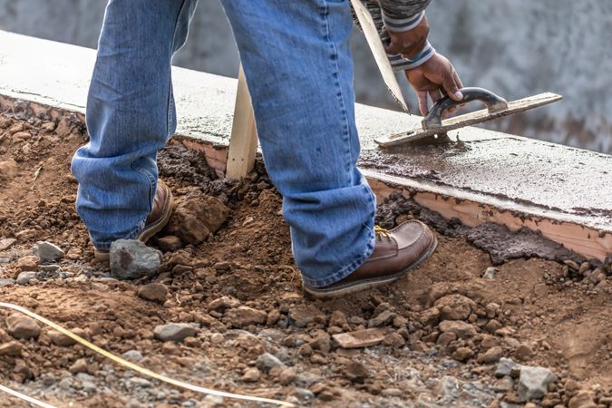 Construction Worker Using Wood Trowel On Wet Cement Forming Coping Around New Pool