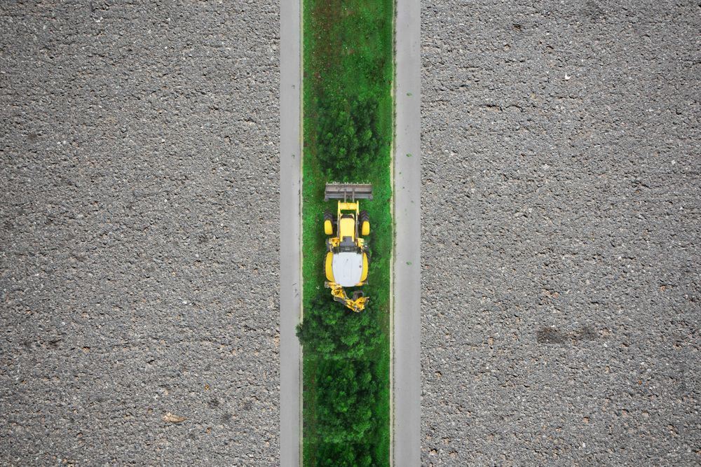 Urban construction, tracktor working on green strip among concrete