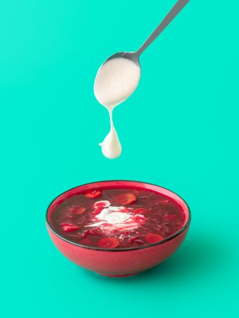 Beetroot soup bowl with sour cream, minimalist on a green background