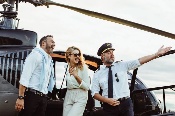 Smiling couple by a private helicopter with pilot