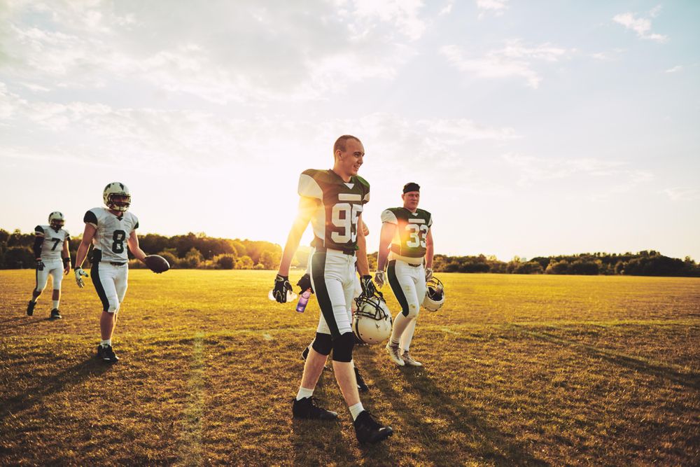 Group of men leaving football pitch after a game at sunset