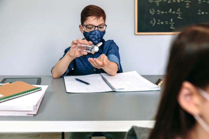 Student with face mask applying hand sanitizer