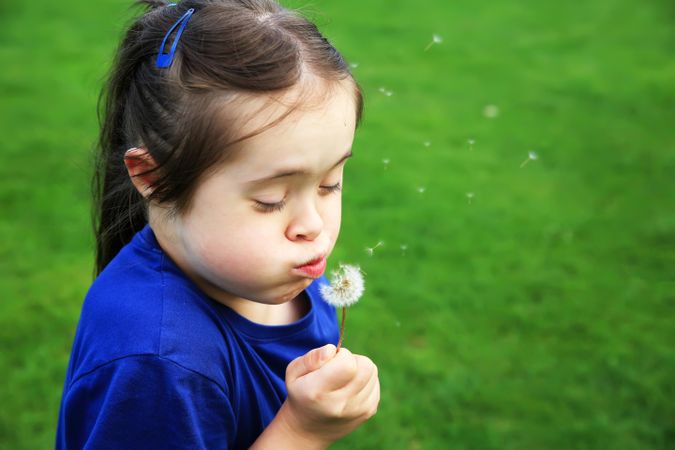 Child blowing dandelion outdoors in a park